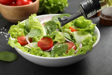 Photo of Pouring oil into delicious vegetable salad on grey table, closeup