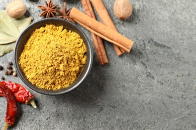 Photo of Dry curry powder in bowl and other spices on dark textured table, flat lay. Space for text