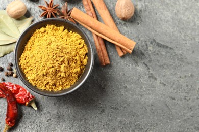 Dry curry powder in bowl and other spices on dark textured table, flat lay. Space for text