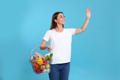 Photo of Young woman with shopping basket full of products on blue background