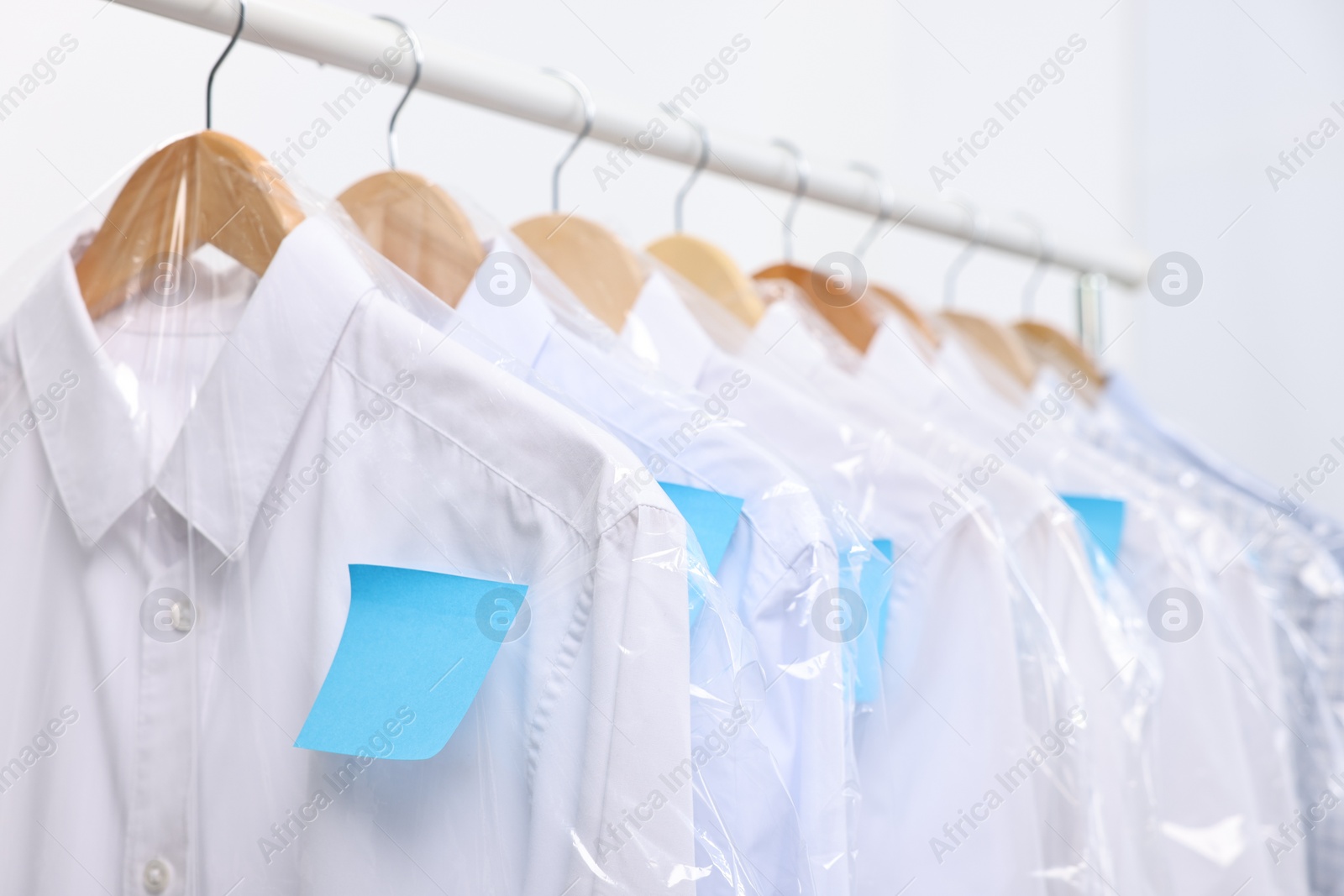 Photo of Dry-cleaning service. Many different clothes in plastic bags hanging on rack against white background, closeup