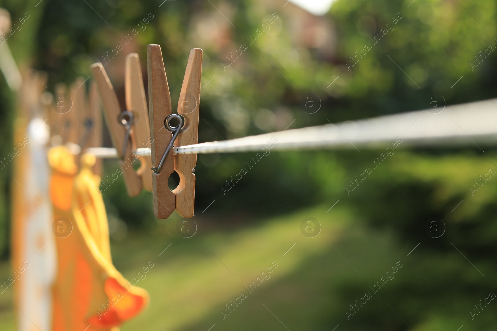 Photo of Clean clothes drying outdoors during sunny day, focus on laundry line with wooden clothespins