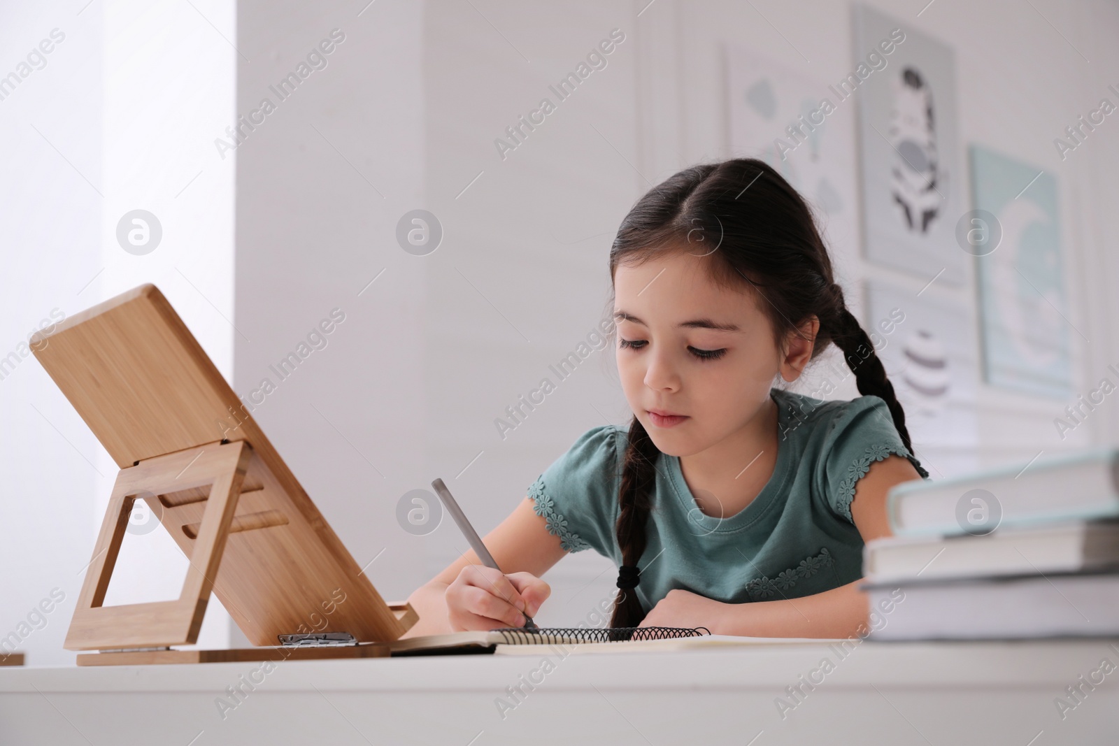 Photo of Little girl doing homework with tablet at table in room