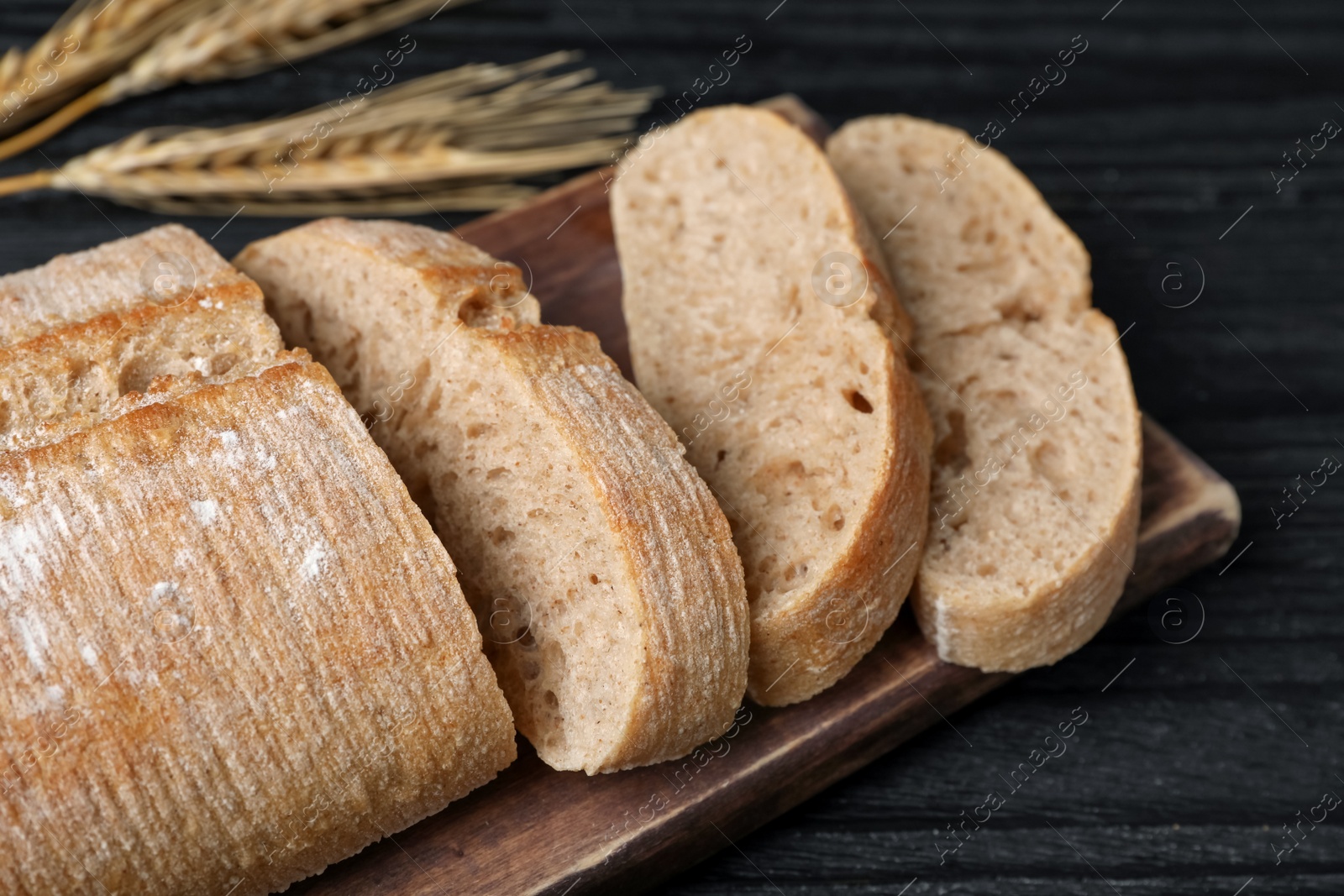 Photo of Cut delicious ciabatta on black wooden table, closeup