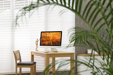 Modern PC on table near window with blinds in room