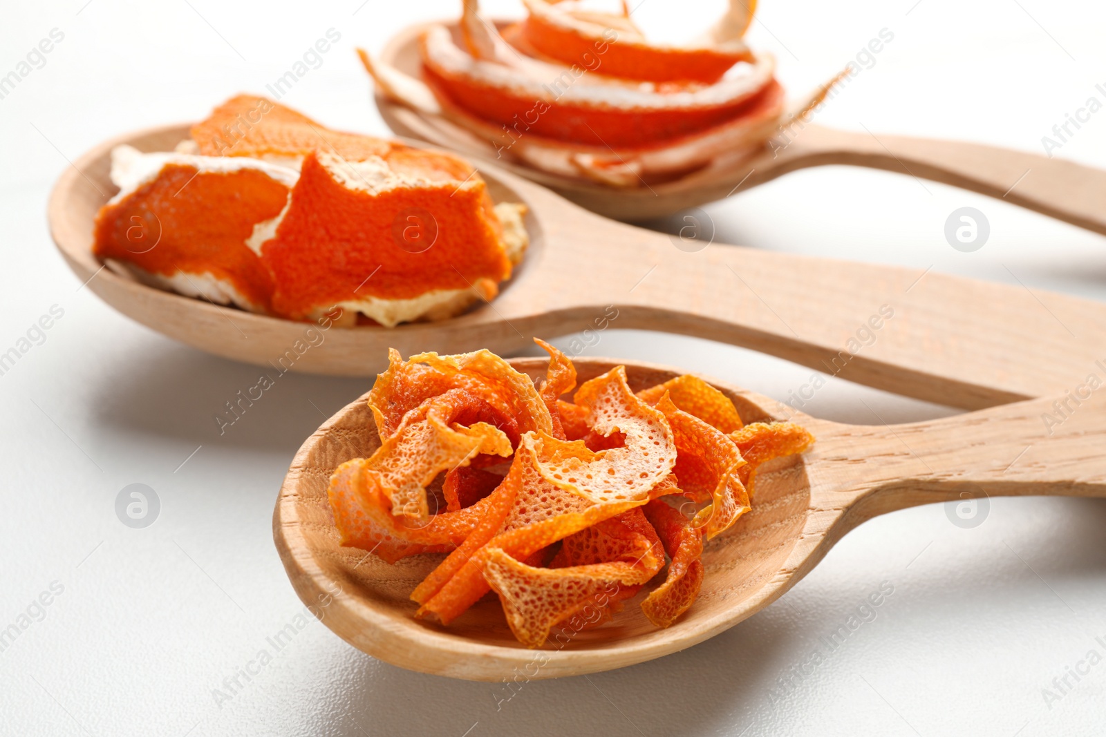 Photo of Spoons with dry orange peels on white marble table, closeup