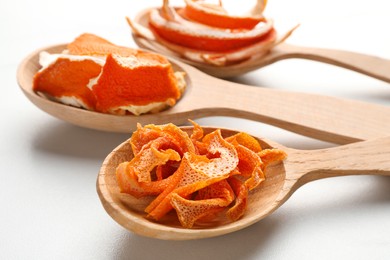 Spoons with dry orange peels on white marble table, closeup