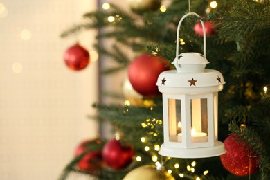 Photo of Christmas lantern with burning candle on fir tree indoors, closeup. Space for text
