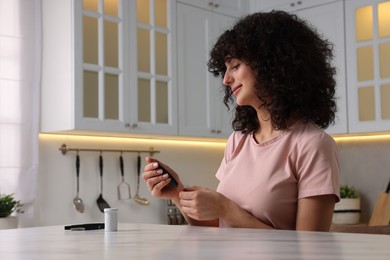 Photo of Diabetes. Woman checking blood sugar level with glucometer at white marble table in kitchen
