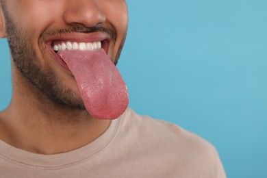 Man showing long tongue on light blue background, closeup