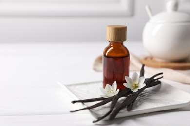 Photo of Vanilla pods, essential oil and flowers on white wooden table, space for text