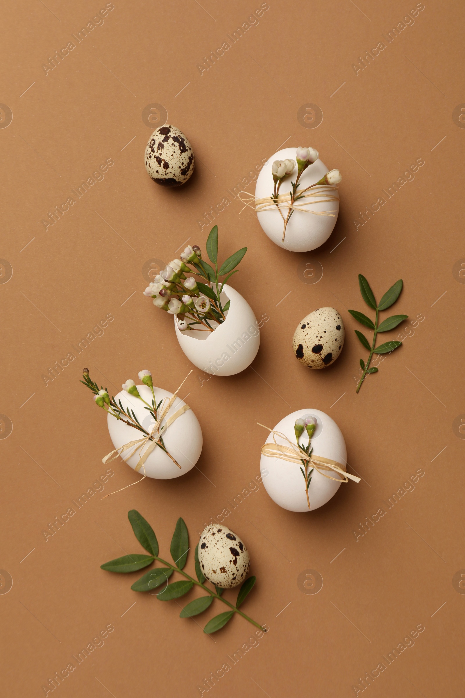 Photo of Festive composition with eggs and floral decor on brown background, flat lay. Happy Easter