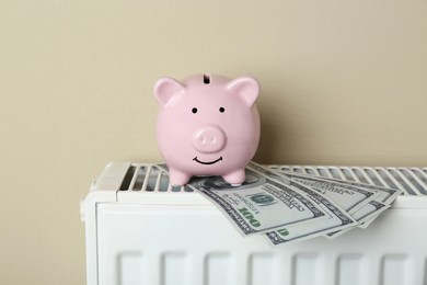 Piggy bank and dollar banknotes on heating radiator against beige background
