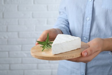 Photo of Woman holding serving board with delicious brie cheese near white brick wall, closeup