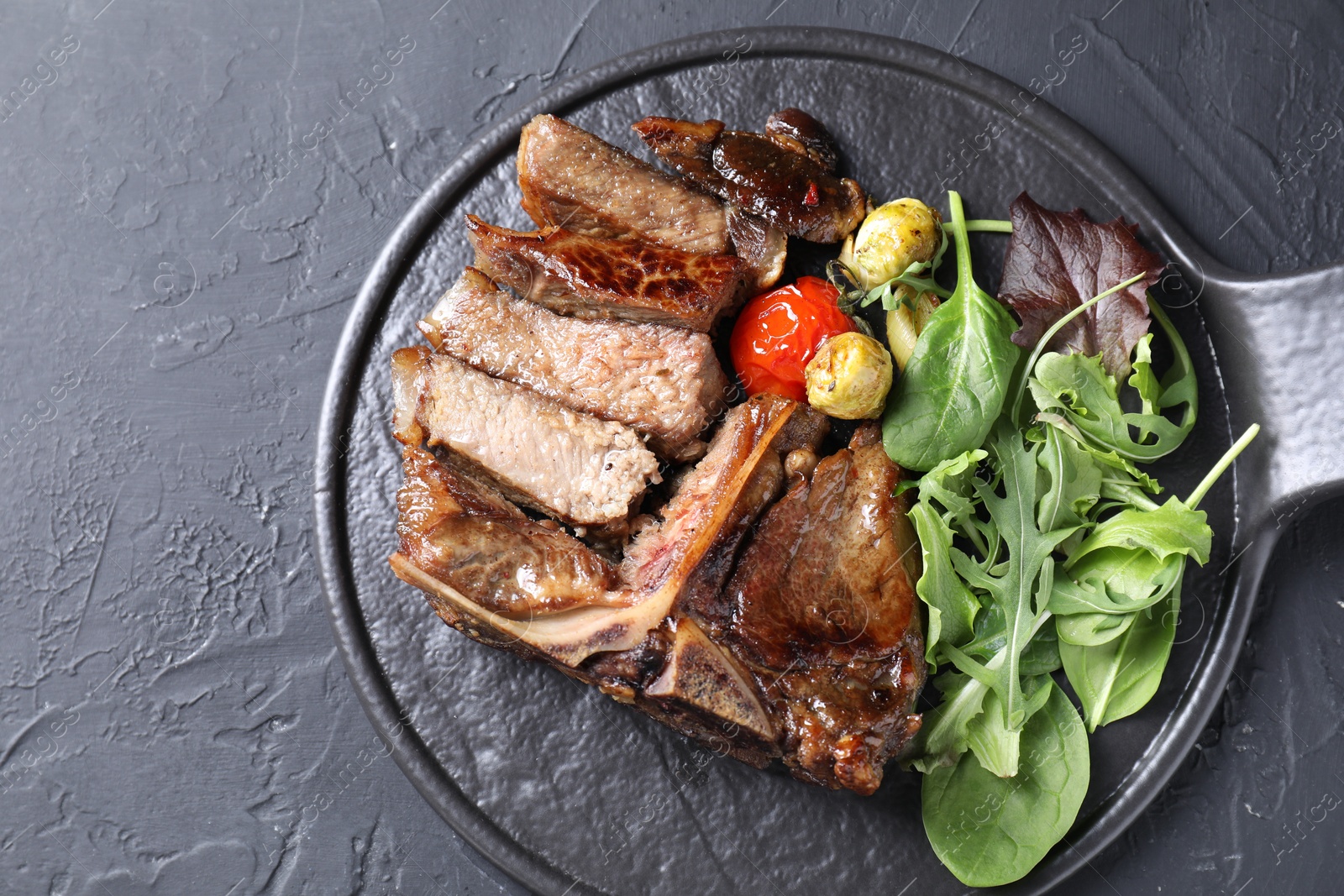 Photo of Delicious grilled beef meat, vegetables and greens on black table, top view