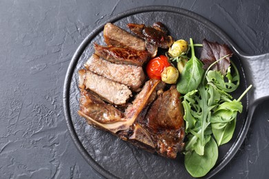 Photo of Delicious grilled beef meat, vegetables and greens on black table, top view