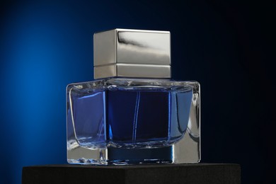 Photo of Luxury men`s perfume in bottle against dark blue background, closeup