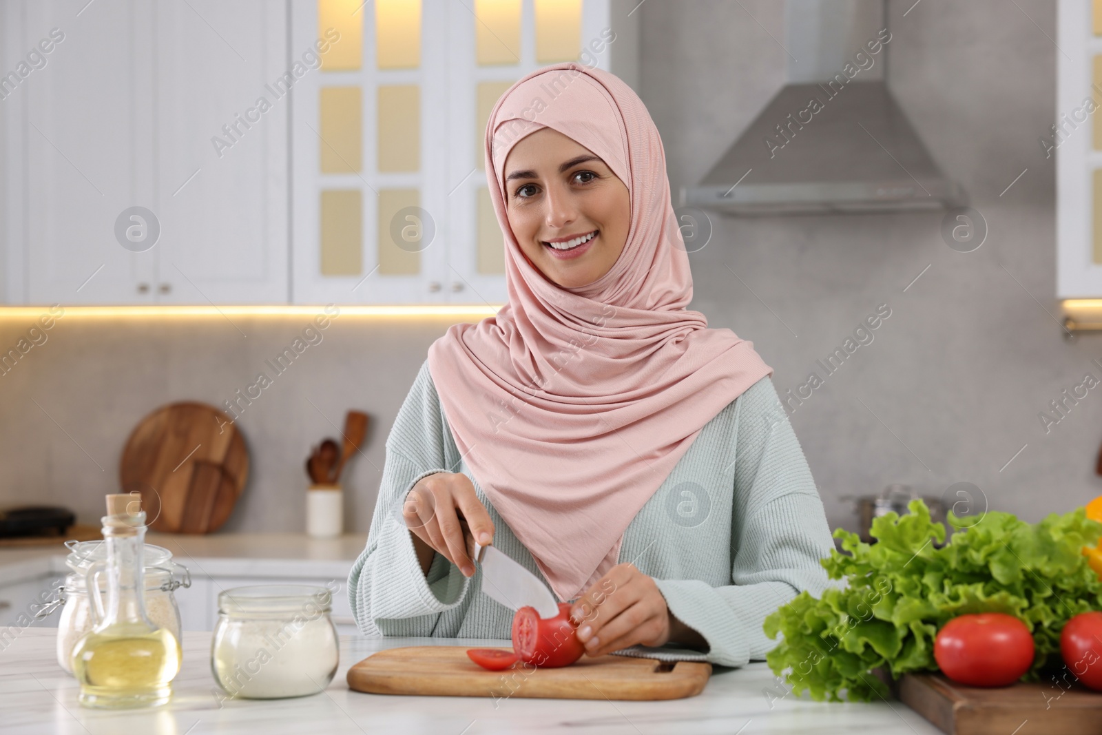 Photo of Muslim woman making delicious salad with vegetables at white table in kitchen