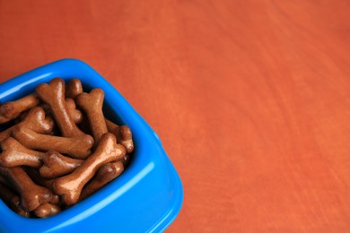 Photo of Blue bowl with bone shaped dog cookies on wooden table, closeup. Space for text