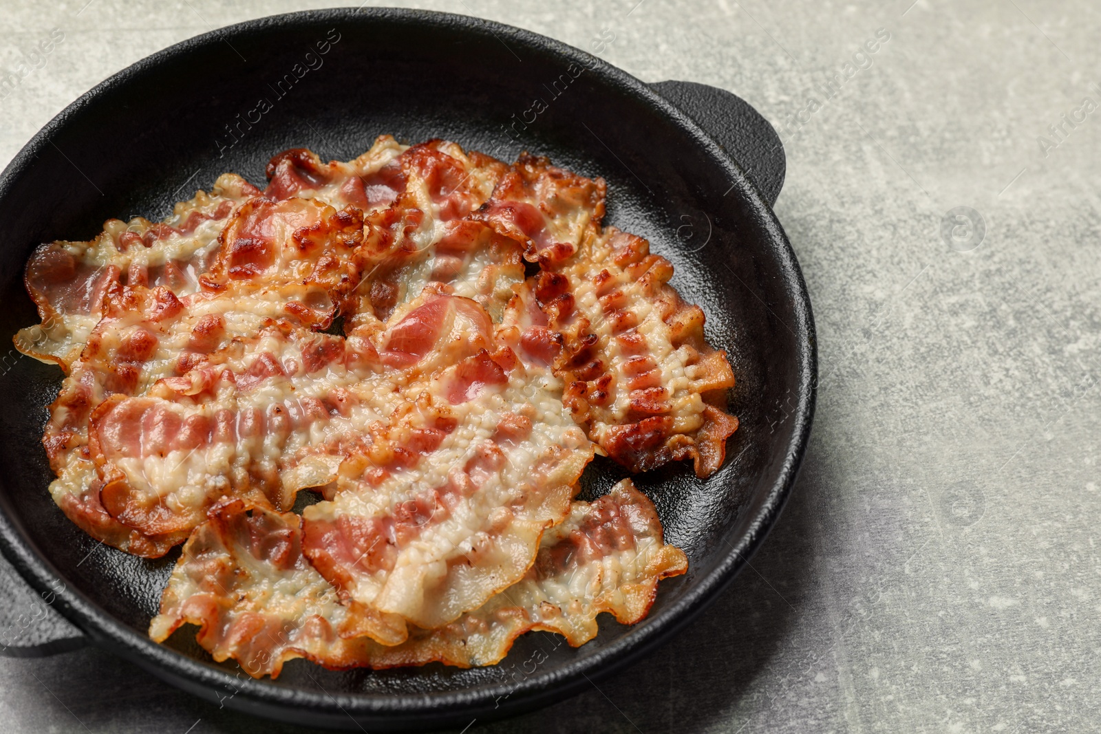 Photo of Delicious bacon slices in frying pan on grey table, closeup