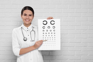 Ophthalmologist pointing at vision test chart near white brick wall, space for text