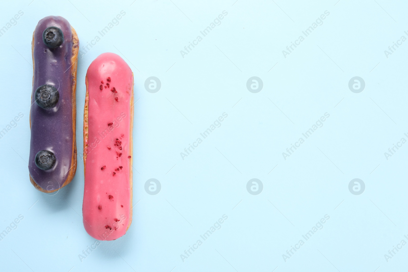 Photo of Delicious eclairs covered with glaze on light blue background, top view. Space for text