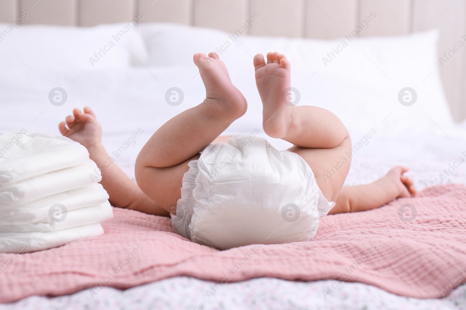 Photo of Little baby and stack of diapers on bed, closeup