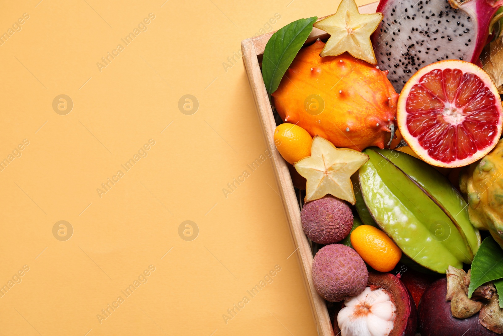 Photo of Different tropical fruits in wooden box on yellow background, top view. Space for text