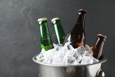 Metal bucket with bottles of beer and ice cubes on grey background