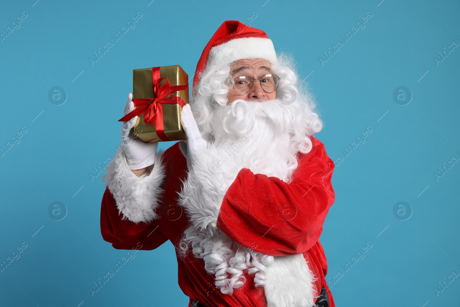 Photo of Santa Claus holding Christmas gift on light blue background