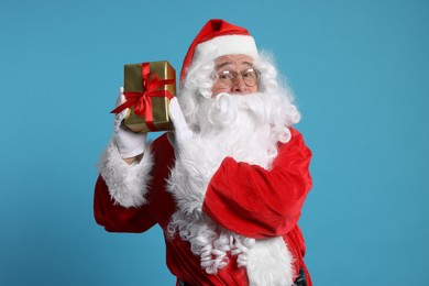 Photo of Santa Claus holding Christmas gift on light blue background