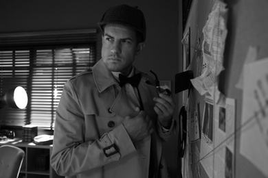 Old fashioned detective with smoking pipe near investigation board in office. Black and white effect