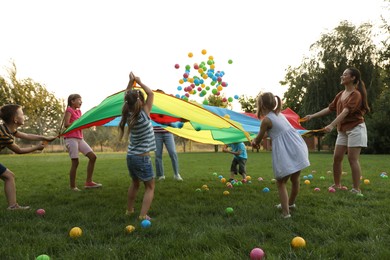 Photo of Group of children and teacher playing with rainbow playground parachute on green grass. Summer camp activity