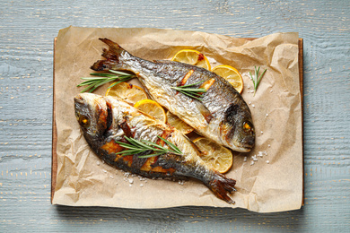 Photo of Delicious roasted fish with lemon on grey wooden table, top view