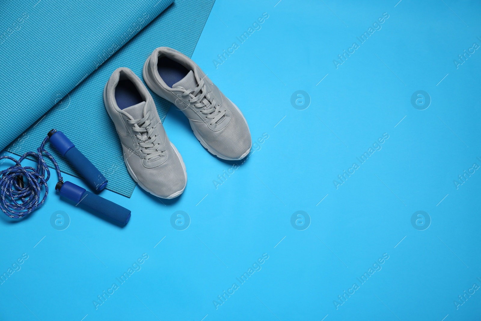 Photo of Exercise mat, shoes and skipping rope on turquoise background, flat lay. Space for text
