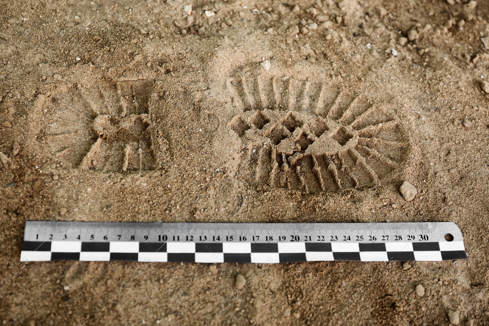 Photo of Ruler near footprint on sand, top view. Crime scene investigation and detective work