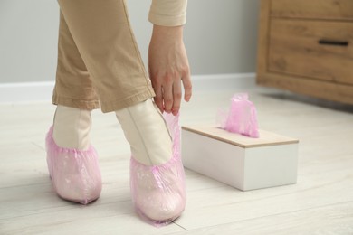 Photo of Woman wearing pink shoe covers onto her boots indoors, closeup