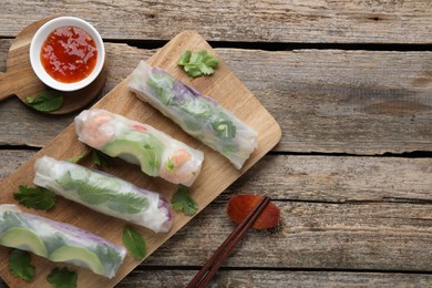 Photo of Delicious spring rolls, sauce and chopsticks on wooden table, top view. Space for text