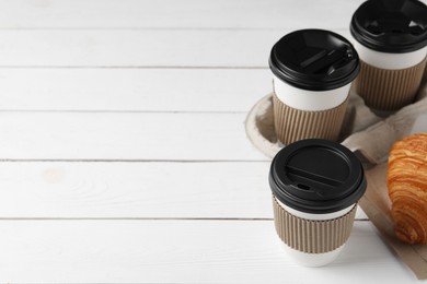 Photo of Coffee to go. Paper cups with tasty drink and croissant on white wooden table. Space for text