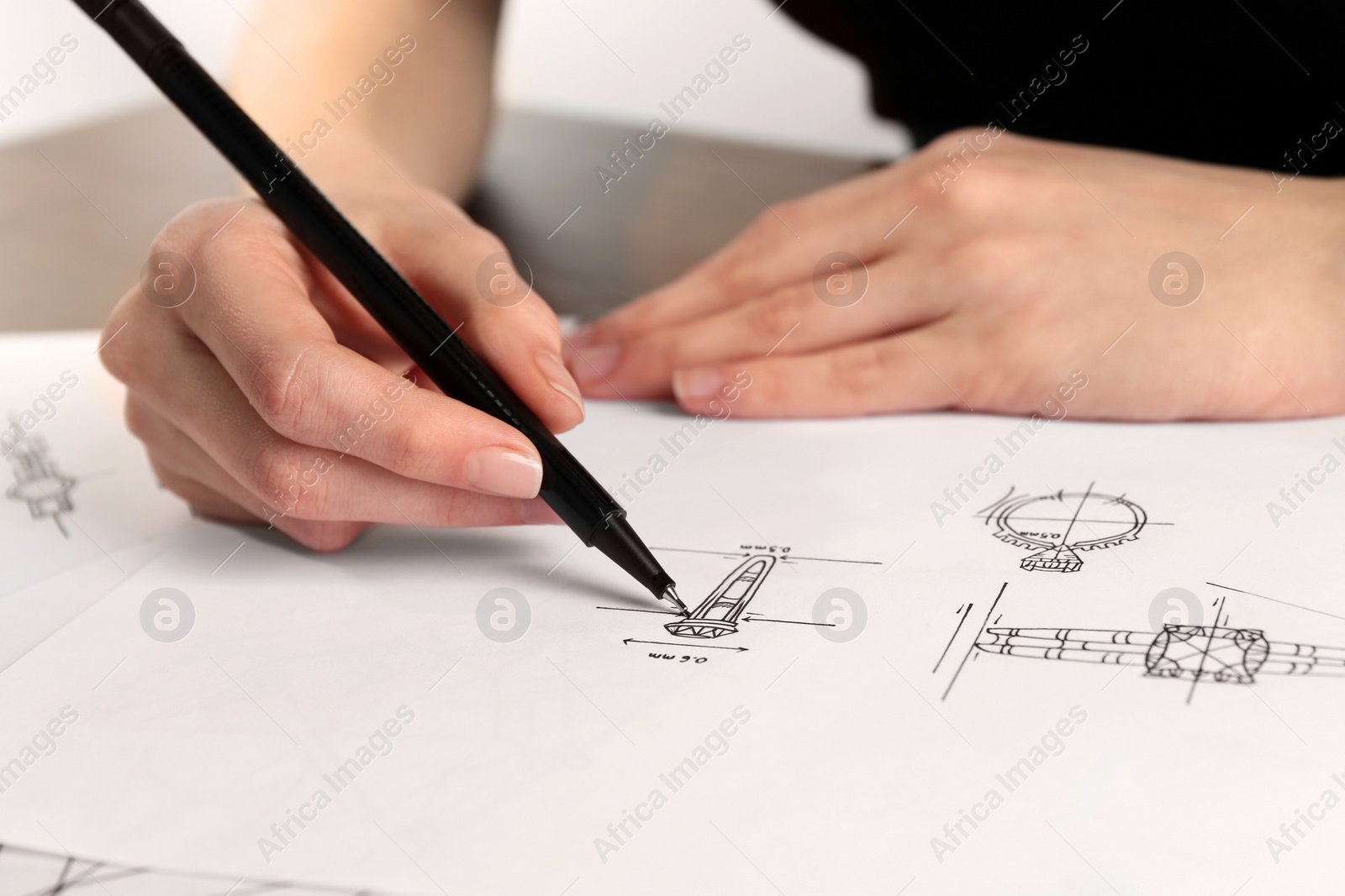 Photo of Jeweler drawing sketch of elegant ring on paper at table, closeup