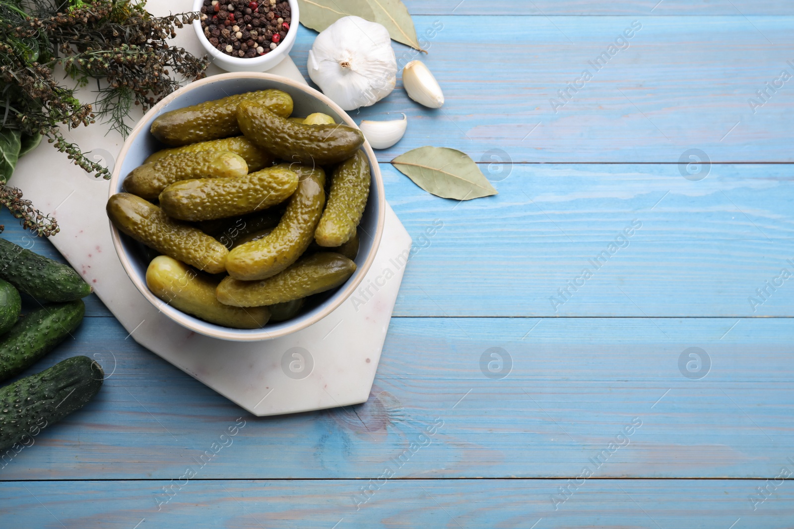 Photo of Fresh and pickled cucumbers with ingredients on light blue wooden table, flat lay. Space for text