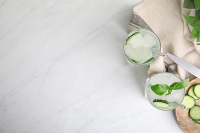Photo of Tasty fresh cucumber water with basil on white marble table, flat lay. Space for text