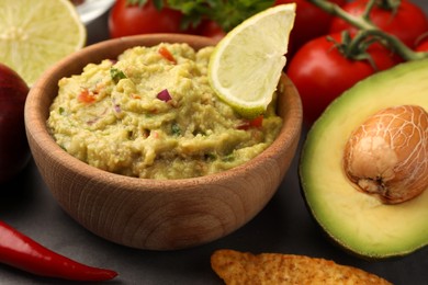 Photo of Bowl of delicious guacamole, nachos chip and ingredients on grey table, closeup