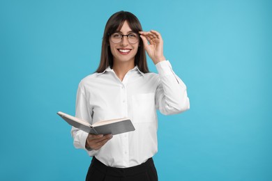 Happy secretary with notebook on light blue background