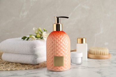 Photo of Stylish dispenser with liquid soap and other bathroom amenities on white marble table