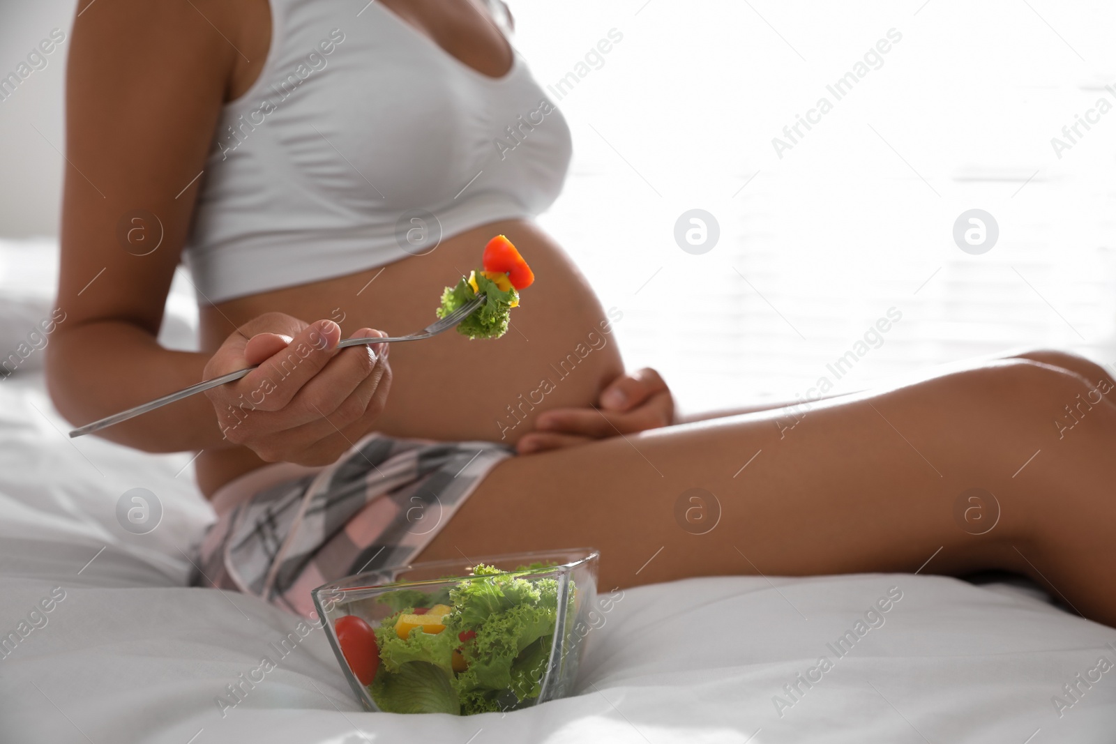 Photo of Young pregnant woman with bowl of vegetable salad in bedroom, closeup. Taking care of baby health