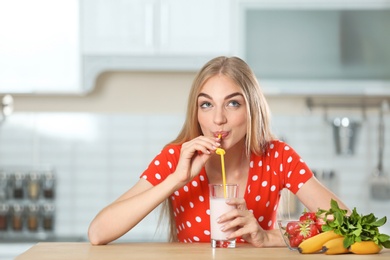 Photo of Young woman with glass of delicious milk shake in kitchen