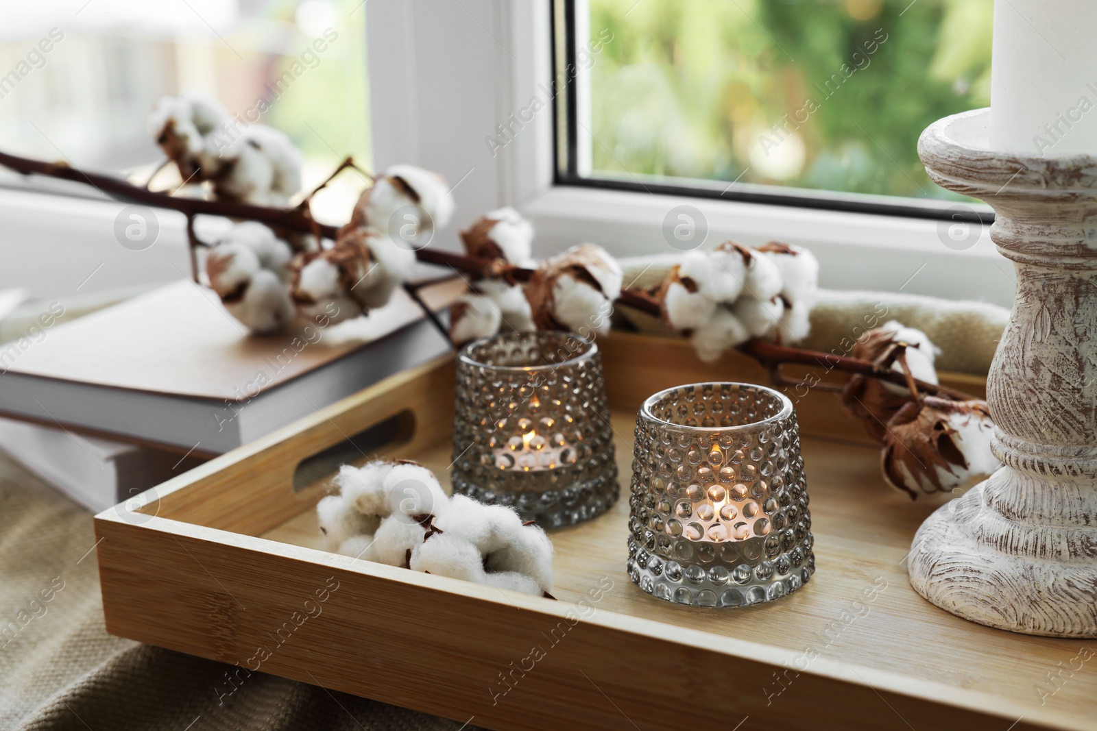 Photo of Beautiful candlestick, scented candles and cotton flowers on wooden tray