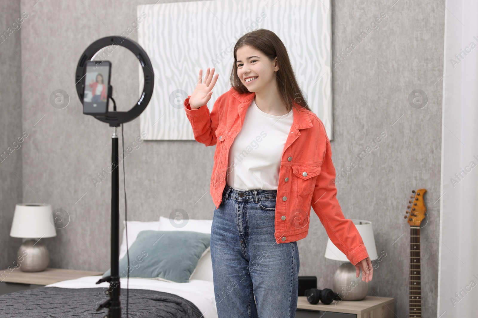 Photo of Smiling teenage blogger waving hello to her subscribers while streaming at home