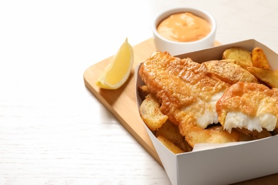 Photo of Disposable container with British Traditional Fish and potato chips on wooden background